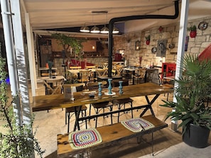 An indoor dining area with wooden tables and benches, stone walls, and potted plants.