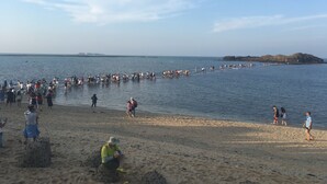 Una playa con gente caminando por la orilla y un área arenosa donde una persona está sentada.