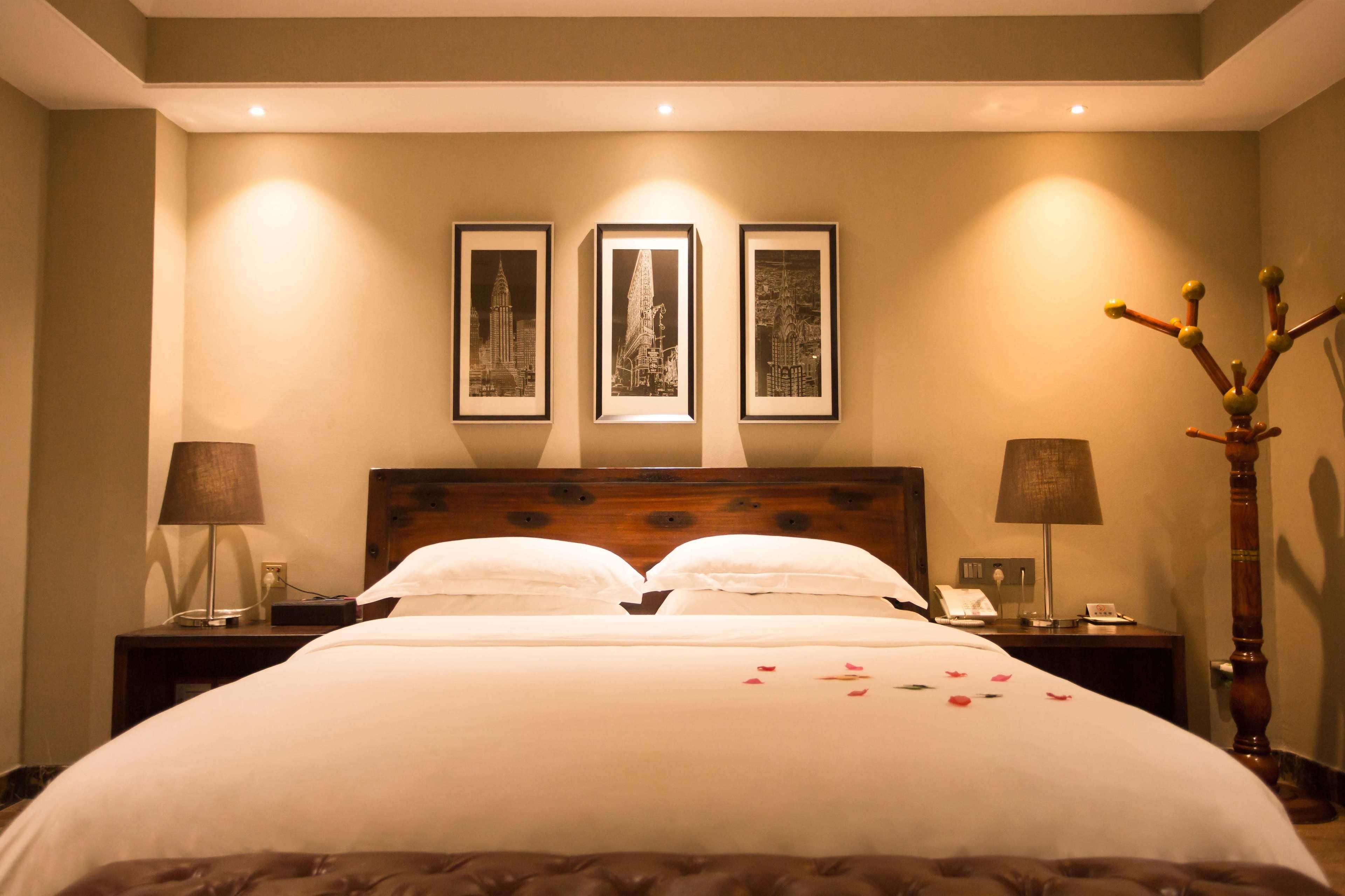 Une chambre d’hôtel avec un grand lit, deux tables de chevet, une petite table, une tête de lit en bois et trois tableaux encadrés accrochés au mur.