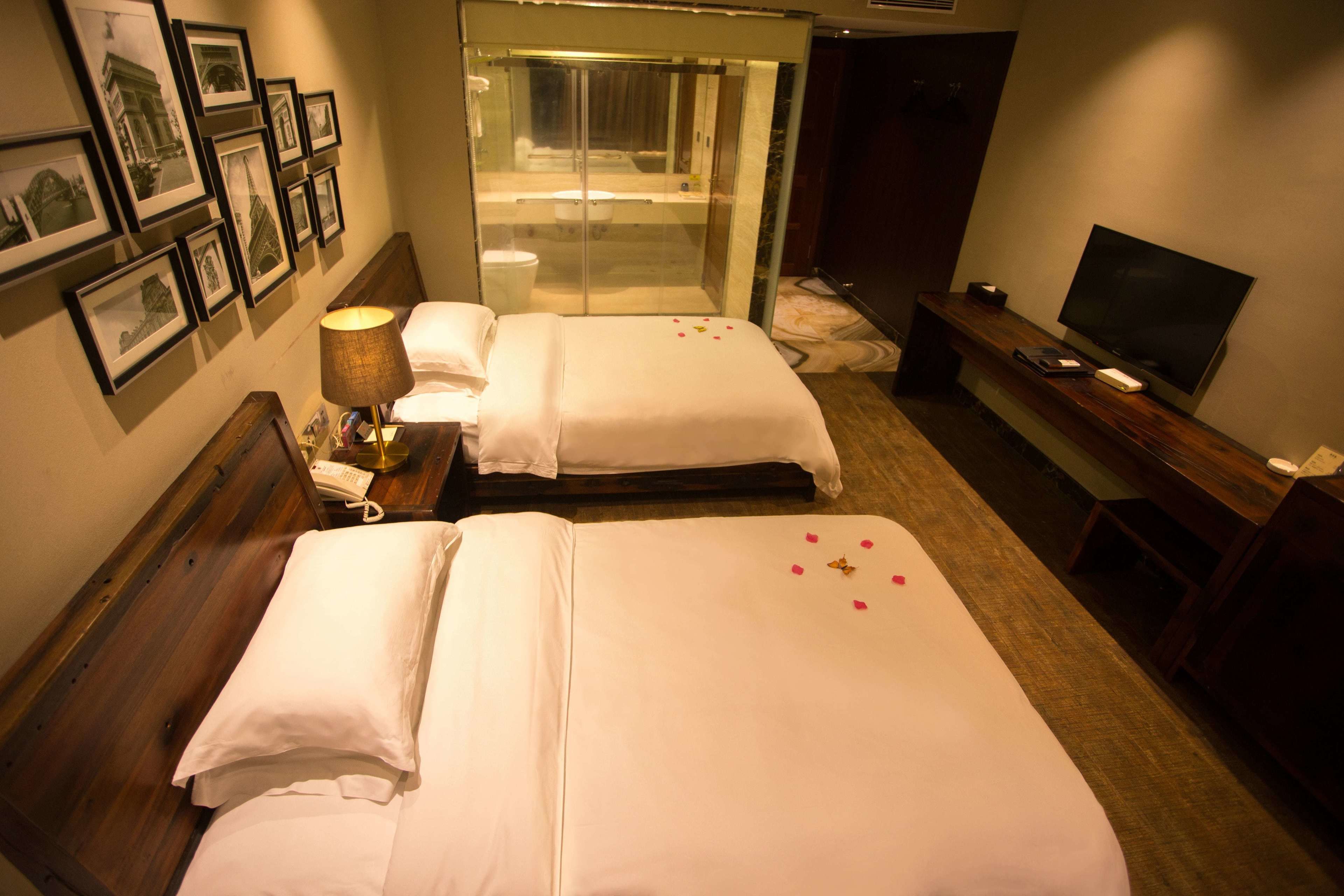 A hotel room with two beds, a shower, a TV, and framed pictures on the wall.