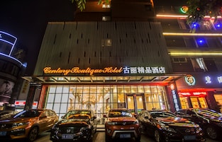 Hotel Century Boutique, con una fachada moderna, varios coches aparcados y señalización iluminada.