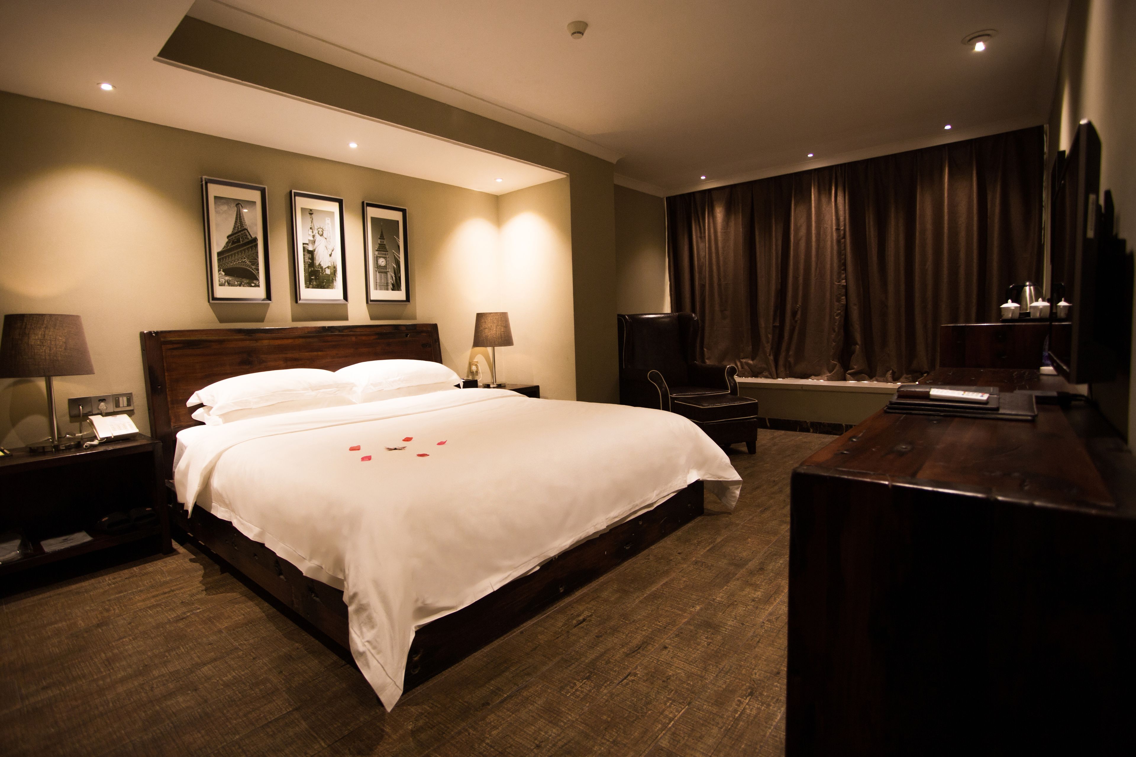 Habitación de hotel con una cama grande, dos mesitas de noche con lámparas, un televisor, un escritorio y una ventana con cortinas.
