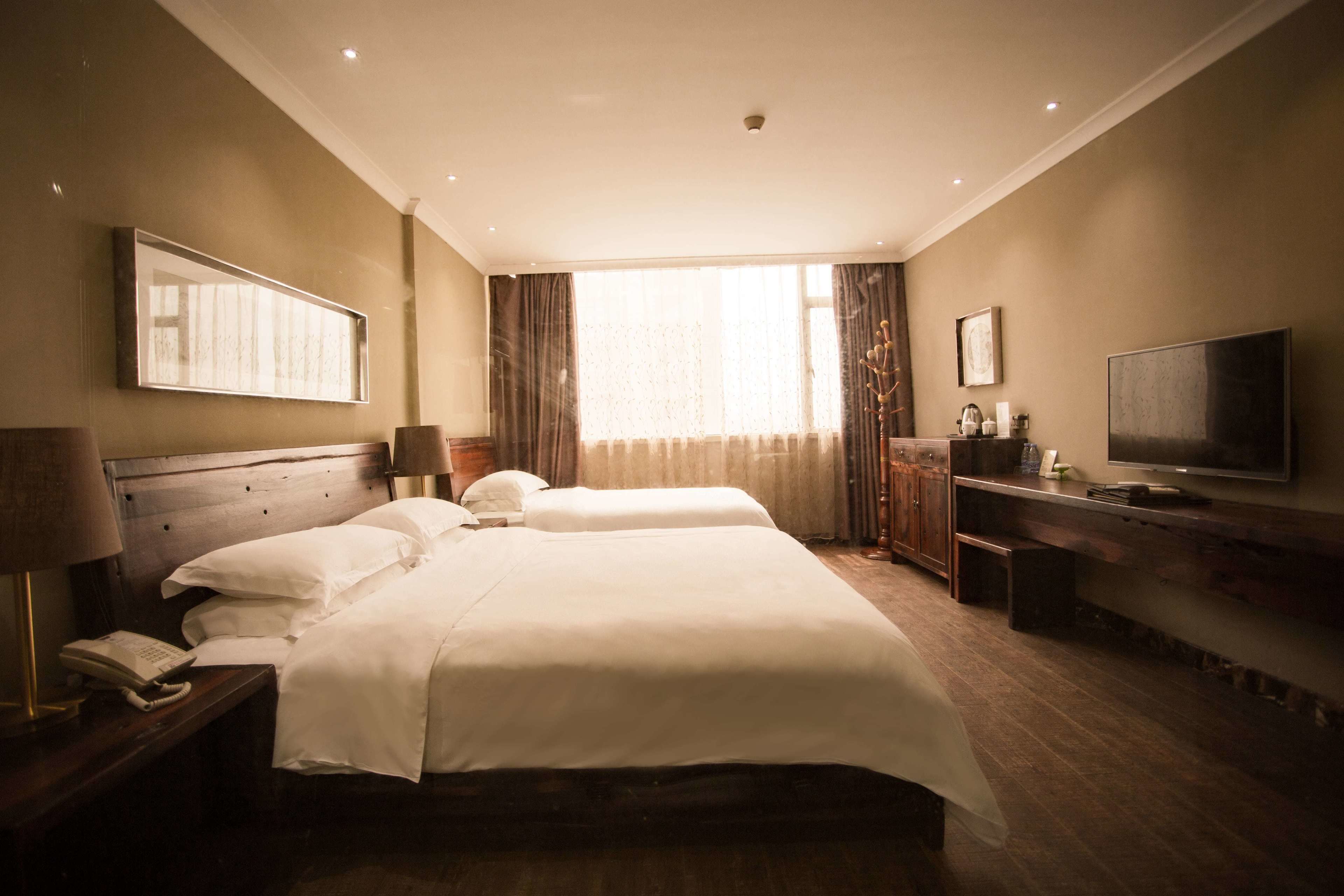 Ein Hotelzimmer mit einem großen Bett, einem Schreibtisch mit Lampe, einem Fernseher und einem Fenster mit Vorhängen.