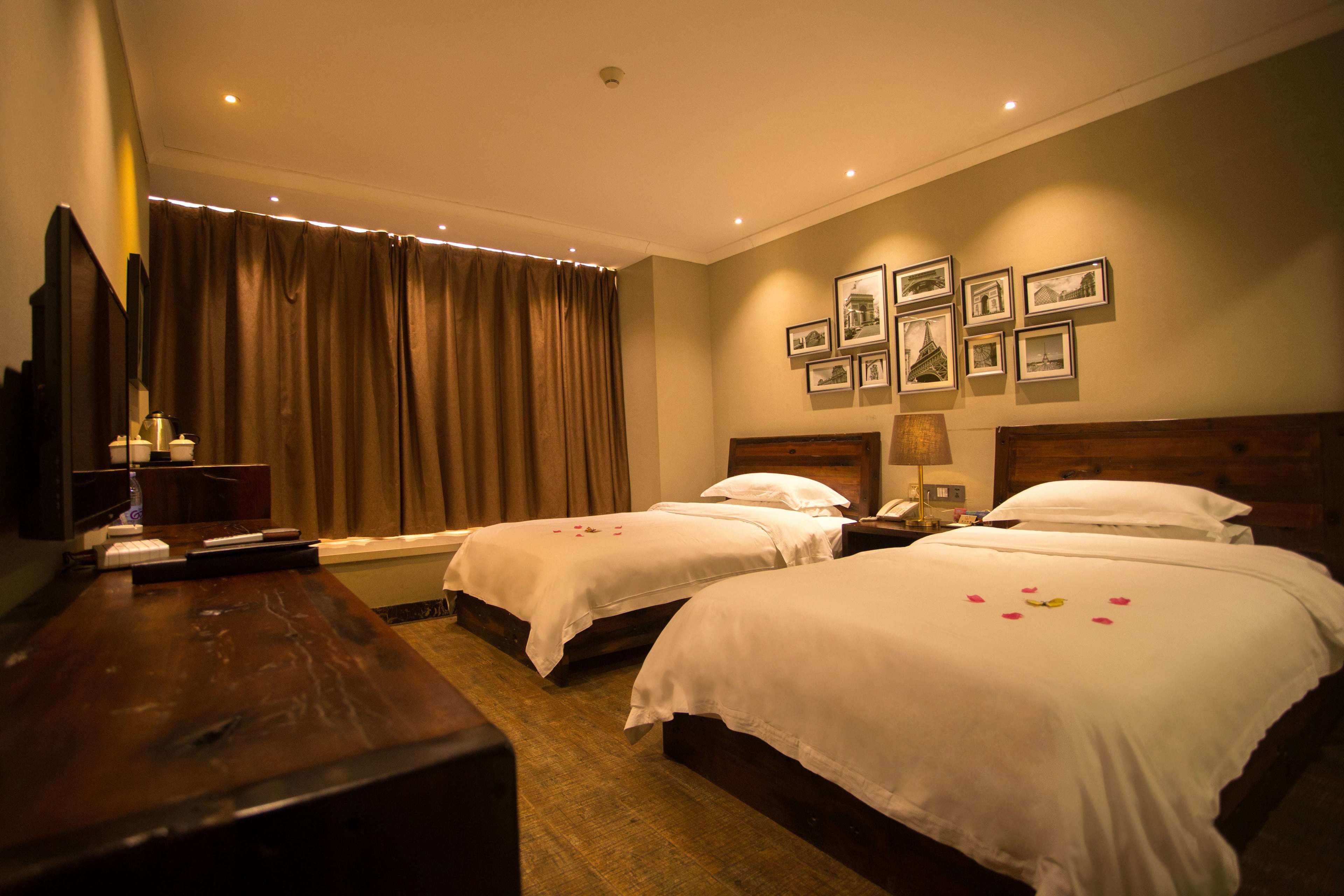 Ein Hotelzimmer mit zwei Betten, einem Holztisch, einem Fernseher und einer Wand mit gerahmten Bildern.