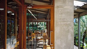 A cafe with wooden furniture, a reception desk, and a view of greenery outside. - SUNKISS pool.bed.cafe (Bangkok)