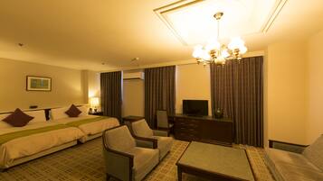 Une chambre d’hôtel comprenant un lit, deux fauteuils, une table basse, une télévision et un bureau.