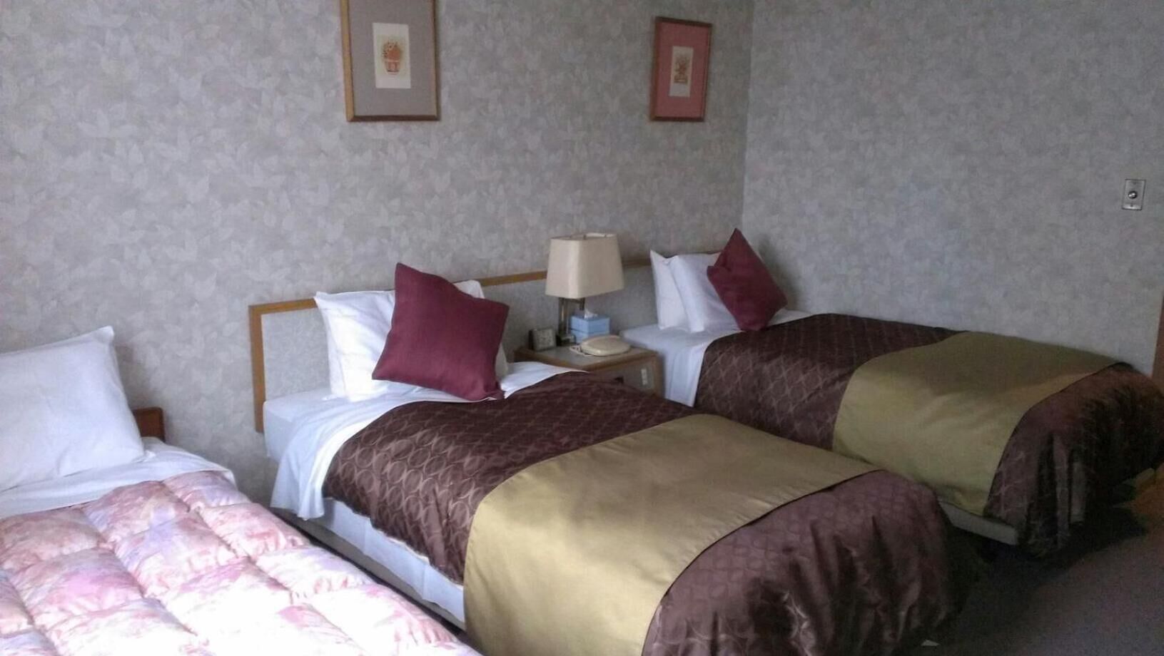 A hotel room with two beds, a nightstand with a lamp, and two framed pictures on the wall.