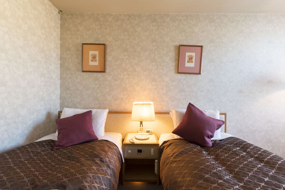 A hotel room with two beds, a nightstand with a lamp, and framed pictures on the wall.