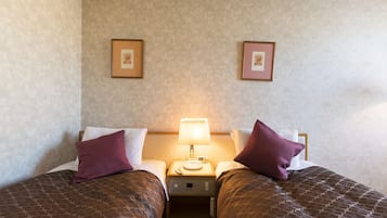 A hotel room with two beds, a nightstand with a lamp, and framed pictures on the wall.