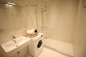 Un baño moderno con lavamanos, lavadora y cabina de ducha de vidrio.