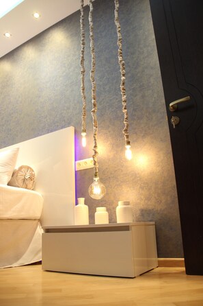 Un dormitorio moderno con una cama blanca, una mesita de noche con botellas y una lámpara de techo original.