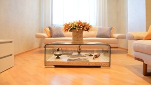 Una sala de estar con una mesa de centro de vidrio, un jarrón con flores y un sofá con cojines.