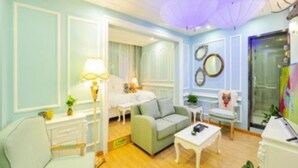 Une pièce comprenant un lit, un canapé vert, un fauteuil blanc, une petite table et une lampe.