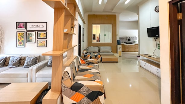 A modern living room with a sofa set, wooden shelving, and a kitchen area in the background. -  Homestay Sawitsari dekat Pakuwon Mall dan UGM by Simply Homy (Depok)