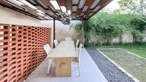 An outdoor patio with a wooden table and chairs, surrounded by a bamboo fence and a garden area. -  Homestay Sawitsari dekat Pakuwon Mall dan UGM by Simply Homy (Depok)