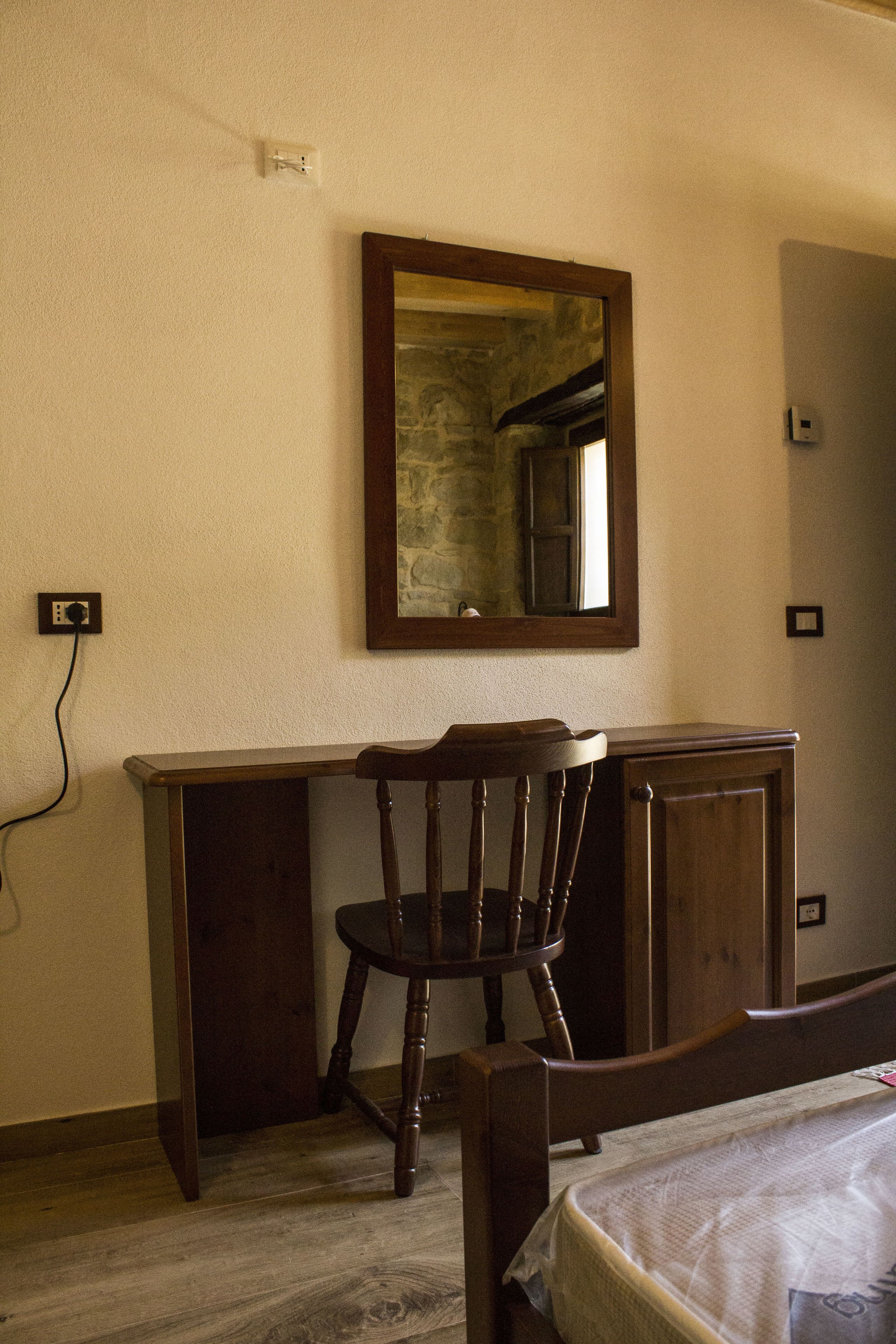 Une pièce avec un bureau en bois, une chaise, un lit et un miroir au mur.