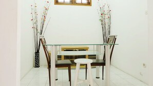 A dining area with a glass-top table, two chairs, and a bench. There are vases with branches and flowers on either side of the table. - Simply Homy Guest House Unit Kaliurang 2 (Ngaglik)