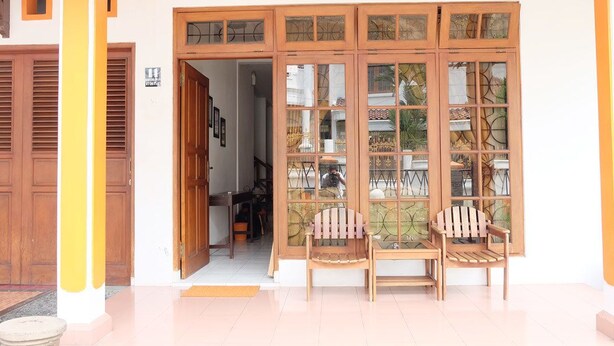 A building entrance with a wooden door, a glass door with a decorative pattern, and two wooden chairs outside. - Simply Homy Guest House Unit Kaliurang 2 (Ngaglik)
