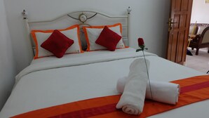 A neatly made bed with white and orange bedding, two red pillows, and a single rose. - Simply Homy Guest House Unit Kaliurang 2 (Ngaglik)