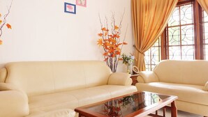 A living room with a beige sofa, a glass coffee table, and a window with curtains. - Simply Homy Guest House Unit Kaliurang 2 (Ngaglik)