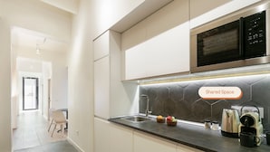 A modern kitchen with white cabinets, a black microwave, and a shared space label. - Arte Suites by Olala Homes (L'Hospitalet de Llobregat)