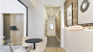 A modern interior with a round table and chairs, a brick accent wall, and a 'Shared Space' sign. - Arte Suites by Olala Homes (L'Hospitalet de Llobregat)