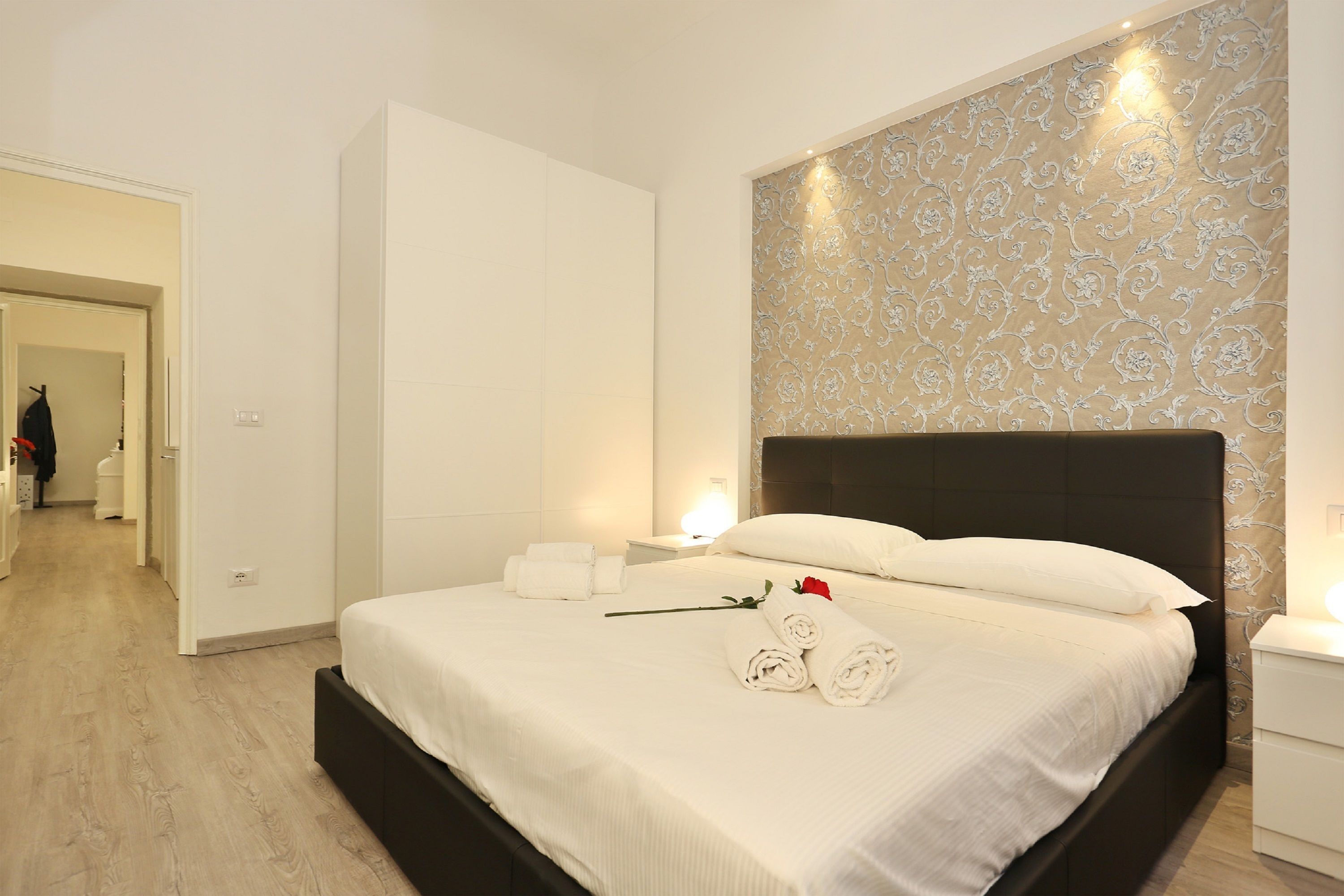 Un lit bien fait, avec des draps blancs, une rose et des serviettes enroulées.