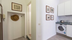 A hallway with a washing machine, a hat, and framed pictures on the wall. - Rental In Rome Beato Angelico Second Apartment (Rome)