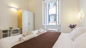 Une chambre d’hôtel équipée d’un lit, d’un bureau, d’une armoire et d’une fenêtre donnant sur des immeubles.
