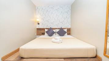 A neatly made bed with a wooden headboard, a wall-mounted light, and a marble-patterned wall.