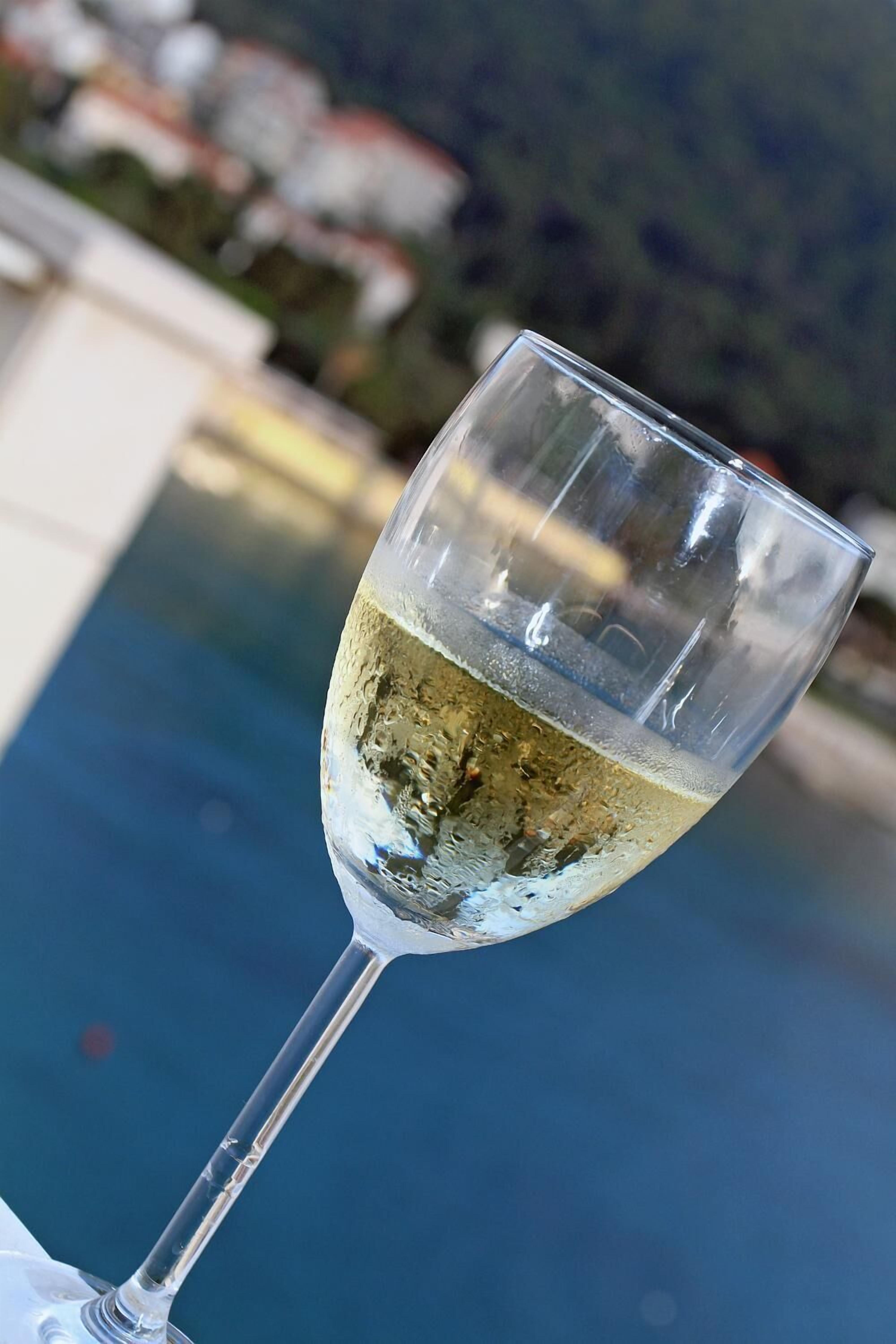 Una copa de vino blanco con una vista despejada de la piscina al fondo.