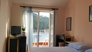 A bedroom with a bed, a desk, a chair, a TV, and a balcony with a view of the sea. - Karla Apartments (Dubrovnik)