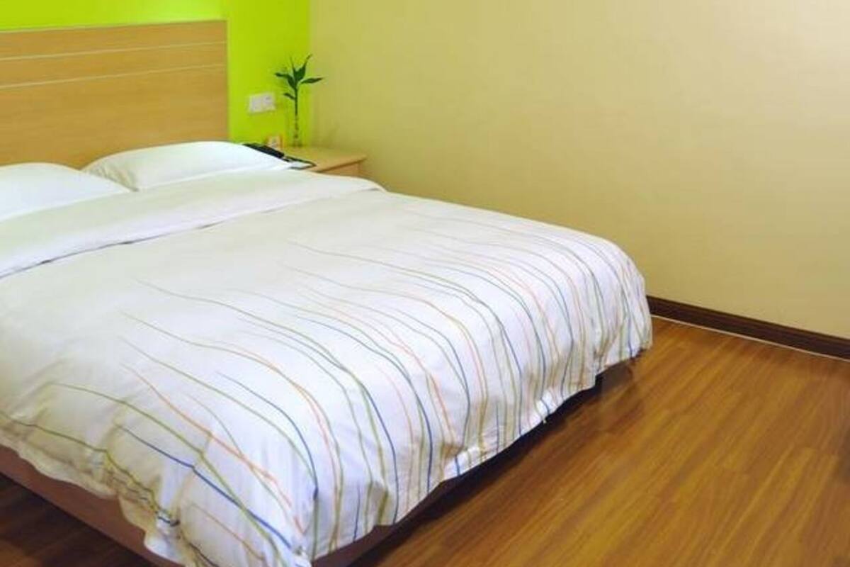 Ein Hotelzimmer mit einem großen Bett, Holzboden, einem Nachttisch mit Lampe und einer Wand mit einem roten und weißen abstrakten Gemälde.