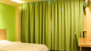 Een hotelkamer met twee bedden, een bureau en een groen gordijn.