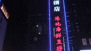 Een gebouw met verlichte borden, waarvan één '恒8连锁酒店' en de andere '港地鲜豆羊4F' vermeldt.