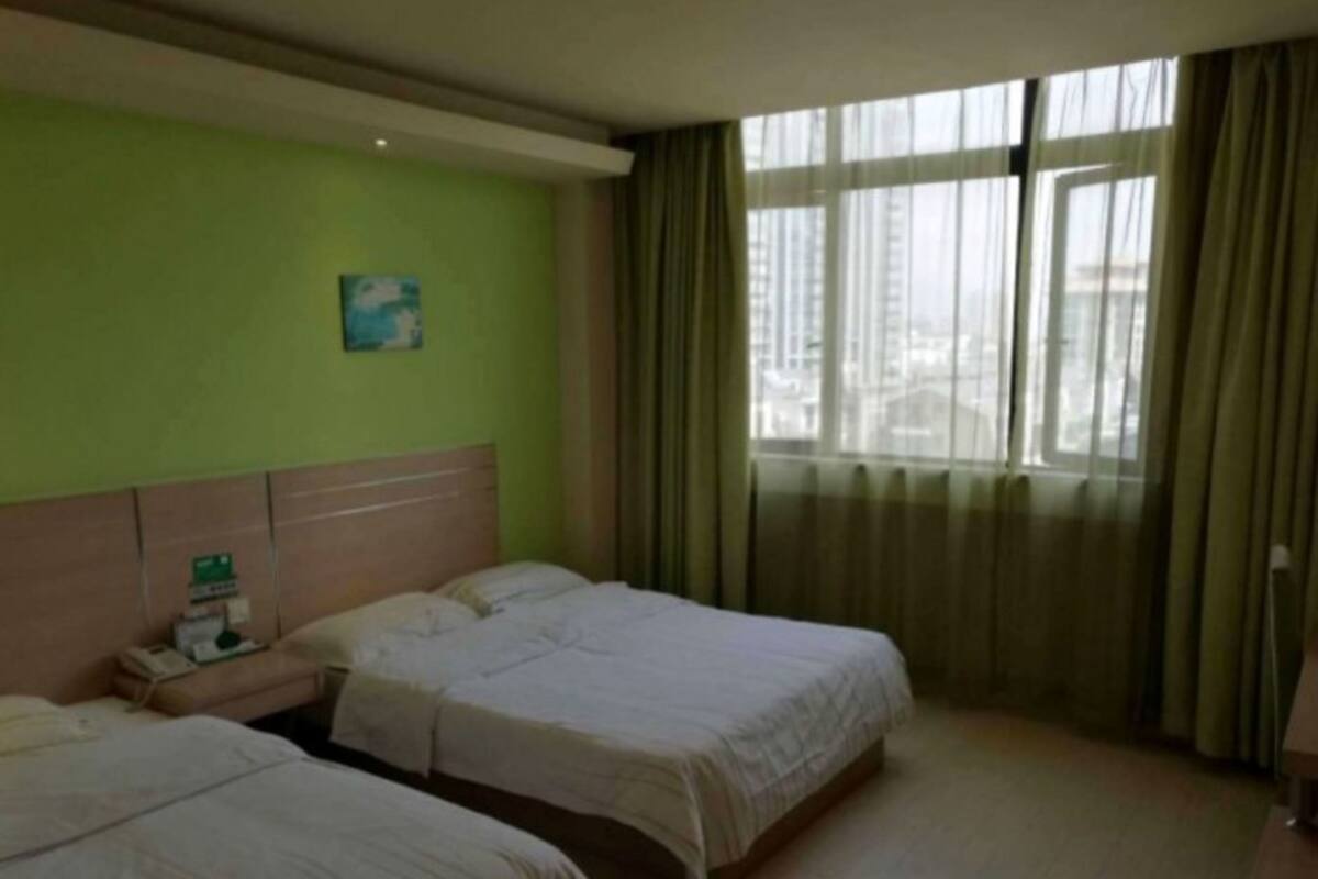 Ein Hotelzimmer mit zwei Betten, einem Nachttisch, einem Fenster mit Vorhängen und einer grünen Wand.