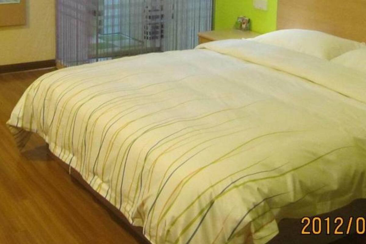 Ein Hotelzimmer mit Bett, grüner Wand und Fenster mit Jalousien.