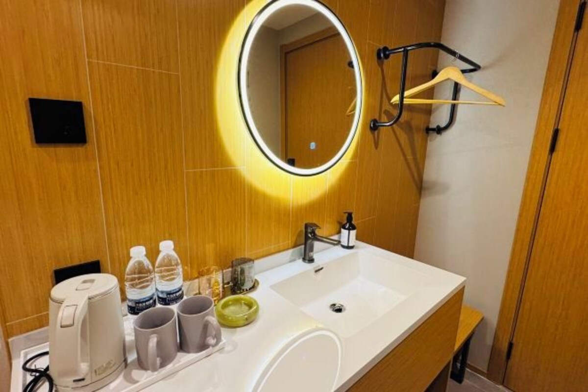 A hotel bathroom with a white sink, a mirror with a light, a towel rack, and a coffee maker.