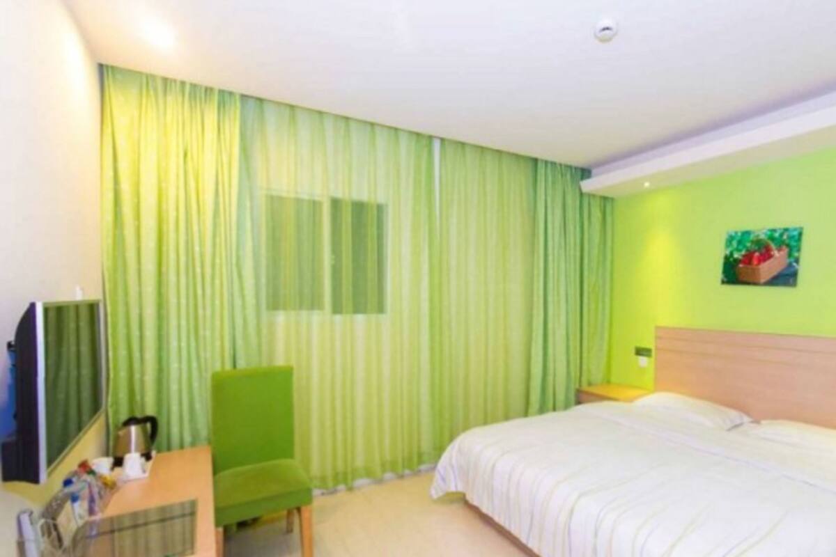 Ein Hotelzimmer mit einem Bett, einem Schreibtisch mit Stuhl, einem Fernseher und einem Fenster mit Vorhängen.