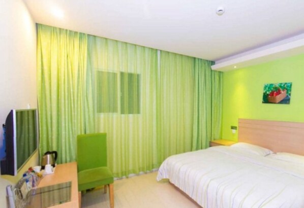 Una habitación de hotel con cama, escritorio, silla, televisor y ventana con cortinas.