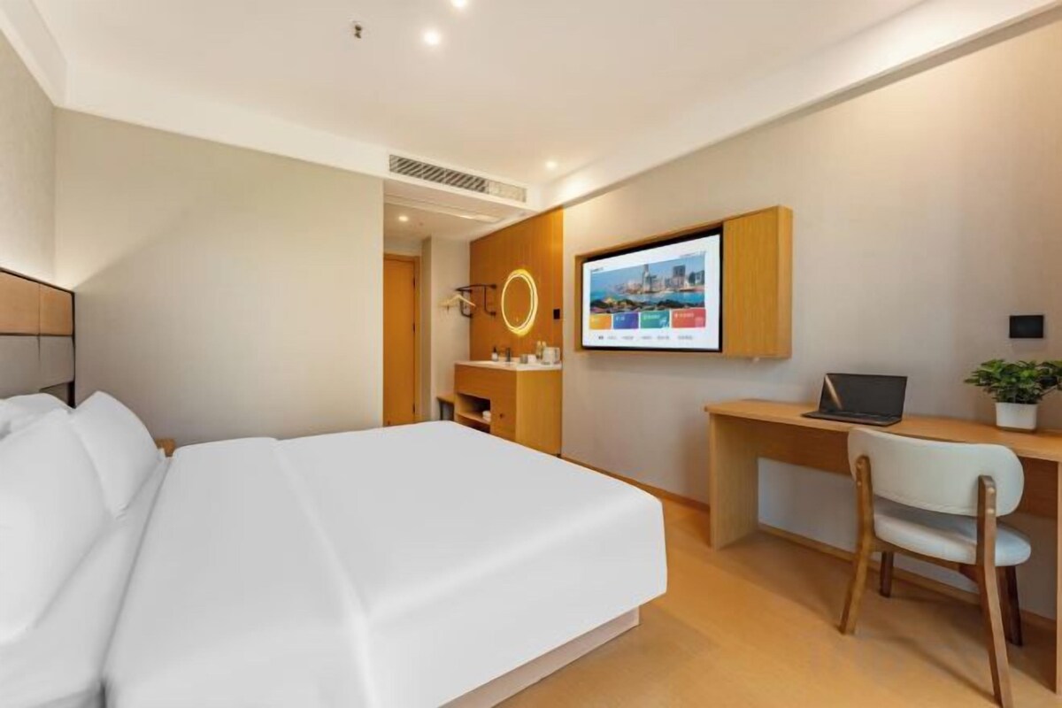 A modern hotel room with a large bed, a desk with a laptop, and a TV mounted on the wall.