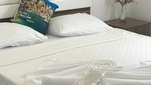 A neatly made bed with white linens, a pillow with a coastal scene, and a small vase with flowers on a bedside table. - Halikarnas Pansiyon (Bodrum)