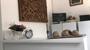 A reception desk with a 'RECEPTION' sign, a wooden wall panel, a clock, a basket of flowers, and a television. - Halikarnas Pansiyon (Bodrum)