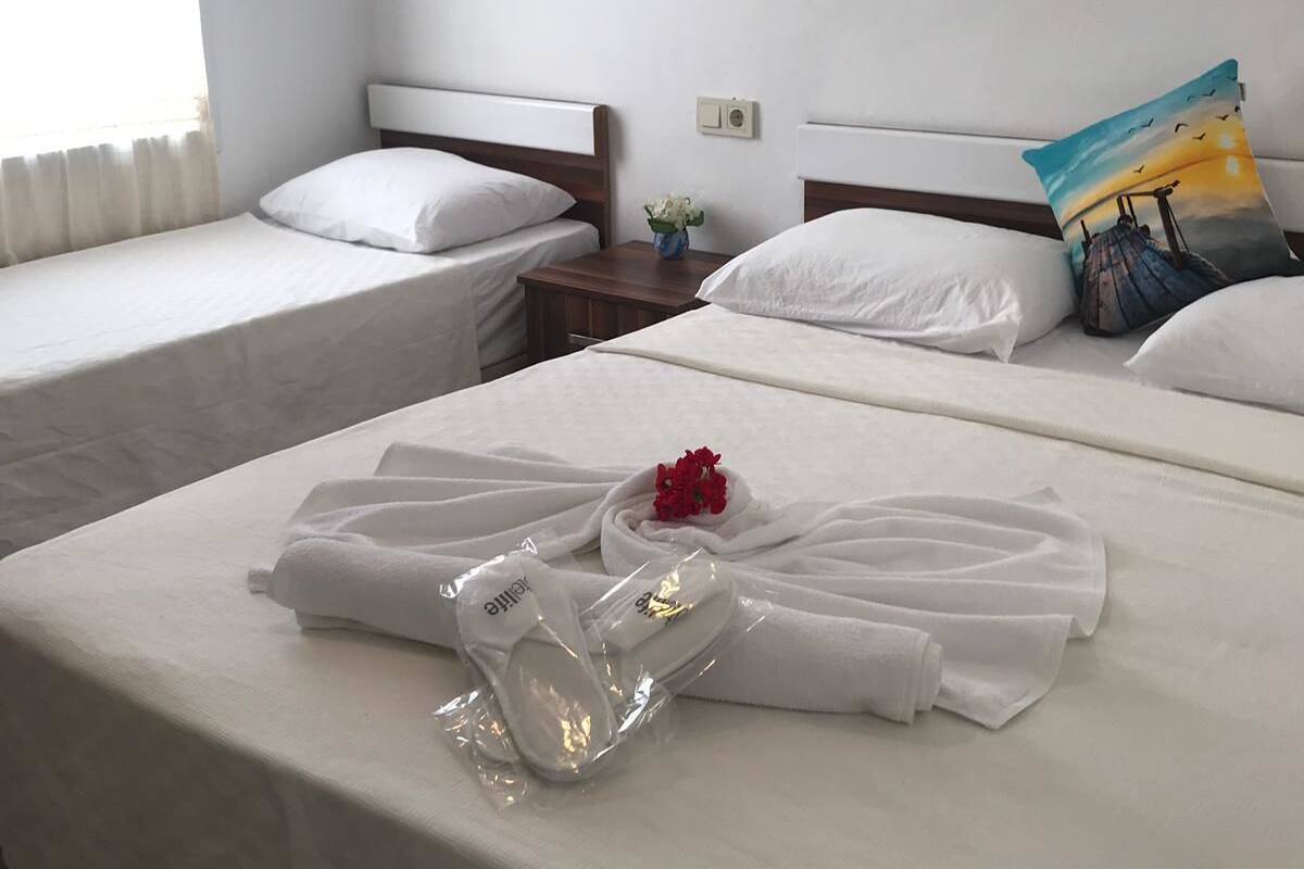 A hotel room with two single beds, a nightstand with a vase of flowers, and a wall-mounted lamp.