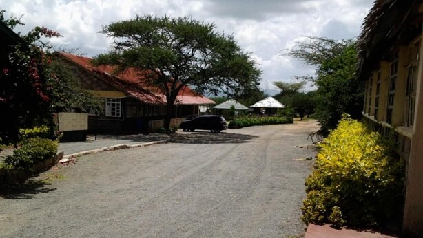 A residential street with houses, a parked car, and a tree. - Kajiado Cultural Resort (Bisil)