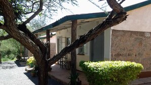 A building with a covered patio area, stone walls, and a well-maintained garden with a trimmed bush. - Kajiado Cultural Resort (Bisil)