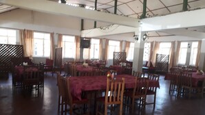 A spacious dining hall with multiple tables and chairs, large windows with curtains, and a high ceiling with exposed beams. - Kajiado Cultural Resort (Bisil)
