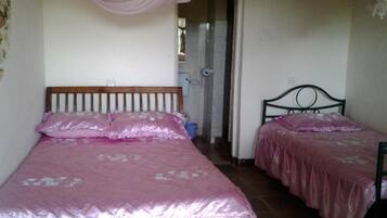Un dormitorio con dos camas, cada una con una colcha rosa y almohadas a juego. Una cama tiene un cabecero de madera y la otra, un cabecero de metal. Una cortina rosa cuelga del techo, y se ve un cubo azul en el suelo.