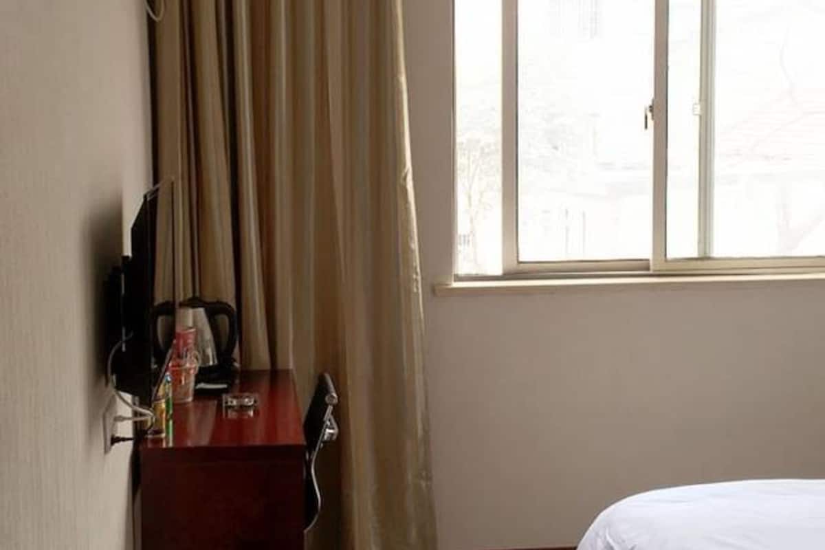 Ein Hotelzimmer mit einem Bett, einem Schreibtisch mit Stuhl, einem Fenster mit Vorhängen und einer Wand-Klimaanlage.