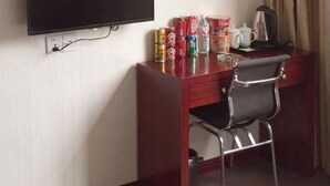 A hotel room with a flat-screen TV mounted on the wall, a wooden desk with a chair, and a minibar with various items. - Wanjing Express Hotel (Hangzhou)